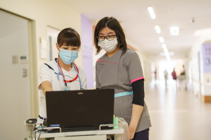 公式看護部ページに掲載された、病棟で情報を確認する看護・介護スタッフ。