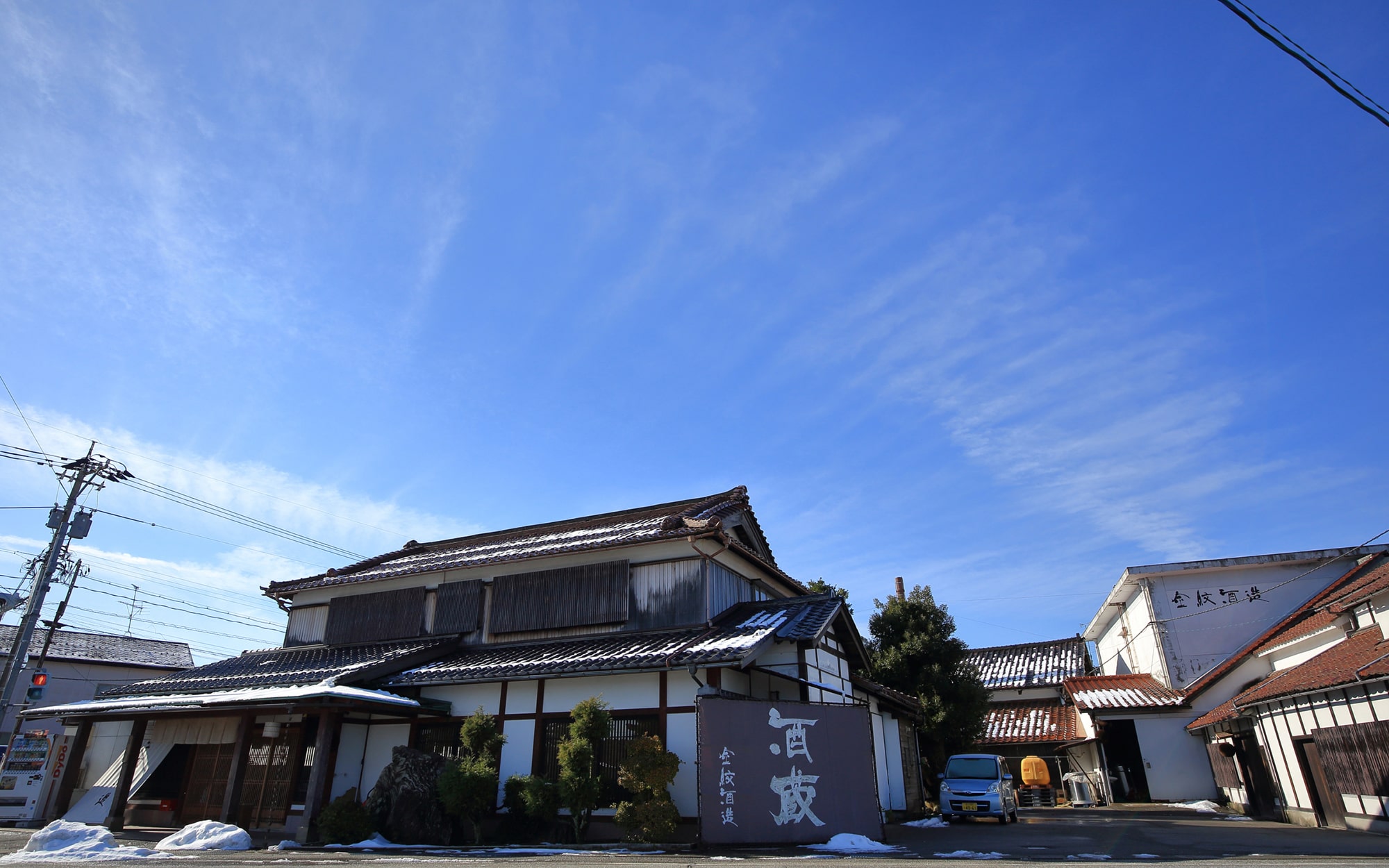 公式トップの「蔵の酒」背景に掲載された、雪の残る酒蔵の外観と西出酒造の看板