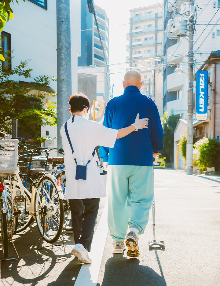 地域の道を歩きながら利用者の動作を支えるスタッフ