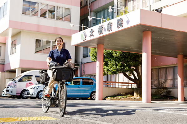 大橋病院の前で自転車に乗る訪問スタッフ