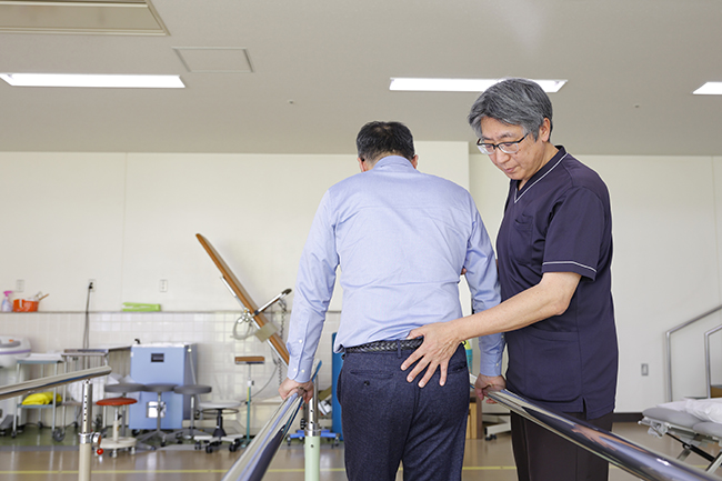 平行棒で歩行訓練を支えるリハビリテーションスタッフ