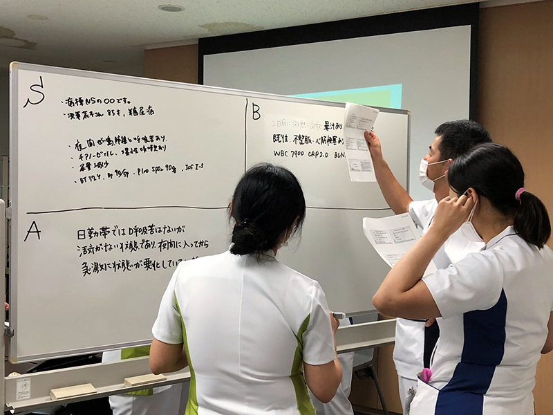 ホワイトボードを囲んで学ぶ看護スタッフ